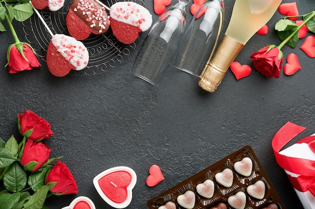 Carta di San Valentino Fiori rossi rosa biscotti brownie e caramelle al cioccolato su confezione regalo a forma di cuore con vino su sfondo nero Biglietto di auguri per la festa della mamma o della donna Vista dall'alto piatto