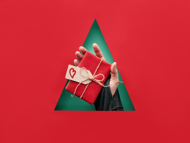 Carta fiamma scarpetta Natale con foro triangolare nel mezzo di carta rossa. Passi la tenuta del regalo di Natale avvolto con cuore sull'etichetta del cartone su fondo verde.