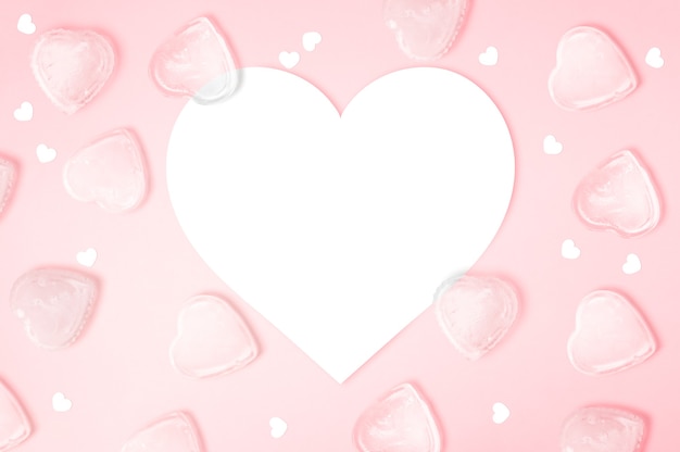 Carta per appunti a forma di cuore con cubetti di ghiaccio su sfondo rosa con spazio di copia, buon san valentino, festa della mamma, piatto laico, vista dall'alto