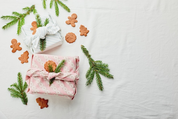 Carta regalo ecologica natalizia in tradizionale stile furoshiki giapponese decorata con ramoscelli di abete e biscotti di panpepato su fondo in tessuto, carta regalo ecologica e concetto Zero Wast
