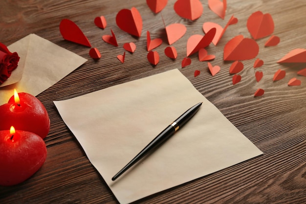 Carta regalo per San Valentino con penna rosa rossa e candele su sfondo di legno