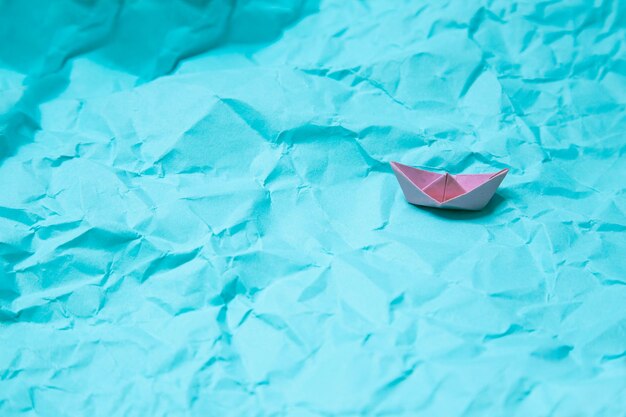 Carta stropicciata che imita il mare con una barchetta di origami rosa. Banner del sito web