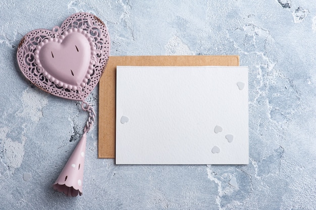 Carta vuota e busta kraft con cuore decorativo rosa. Matrimonio mock up sul tavolo grigio