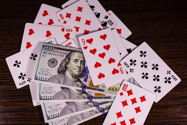 Carte da gioco e banconote da cento dollari su un tavolo di legno scuro