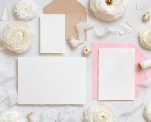 Carte vuote e buste vicino a rose color crema e nastri bianchi mockup matrimonio vista dall'alto