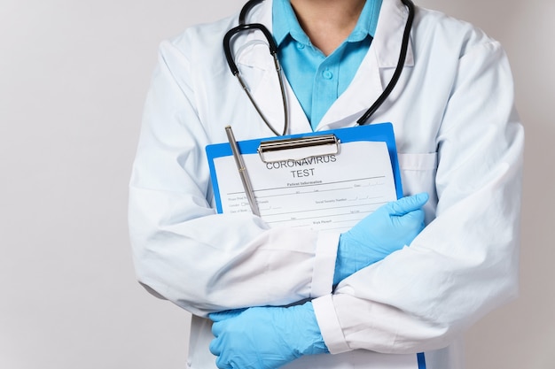 Cartella della tenuta del medico con un modulo di test del coronavirus sul muro grigio