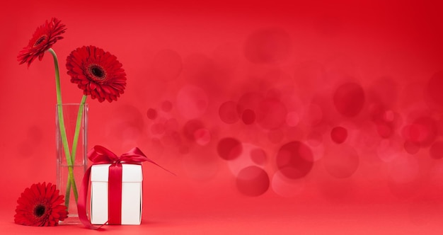 Cartella di auguri per il giorno di San Valentino con fiore di gerbera e scatola regalo davanti a uno sfondo rosso con spazio per i tuoi saluti