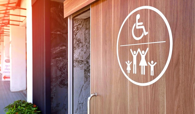 Cartello bianco per sedia a rotelle e bagno per famiglie per disabili sulla porta scorrevole in legno del bagno nell'area pubblica