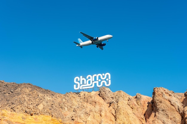 Cartello SHARM sulle rocce sullo sfondo del cielo con aereo Destinazione del viaggio