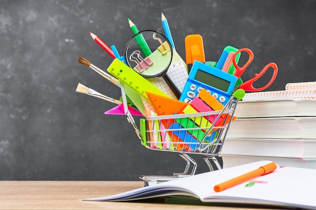 Cartoleria per la scuola in un carrello sullo sfondo di una lavagna