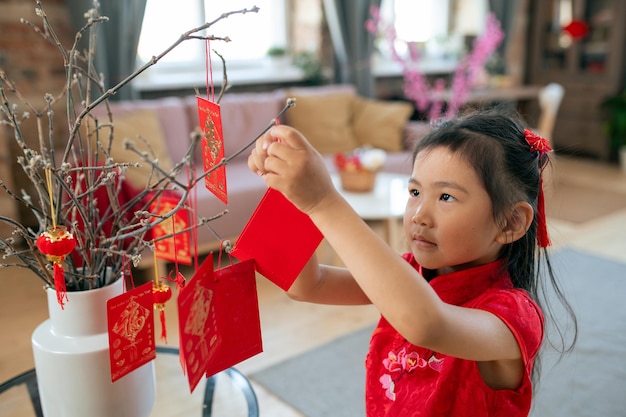 Cartolina d'attaccatura della bambina graziosa con gli auguri del nuovo anno sul ramo