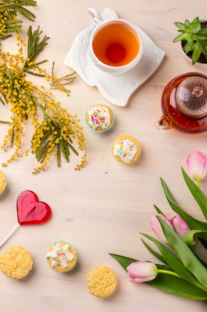 Cartolina d&#39;auguri del giorno delle donne con i tulipani, la mimosa, il tè ed i bigné su fondo di legno.