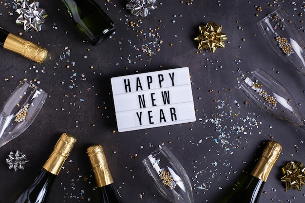 Cartolina d'auguri di felice anno nuovo bicchieri di champagne e coriandoli di bottiglie