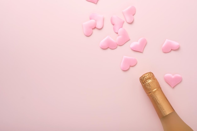 Cartolina d'auguri di San Valentino con bottiglia di champagne, bicchieri di traino, cuori di cioccolato e confezione regalo su sfondo rosa. Vista dall'alto con spazio per i saluti. Biglietto di auguri con spazio per la copia.