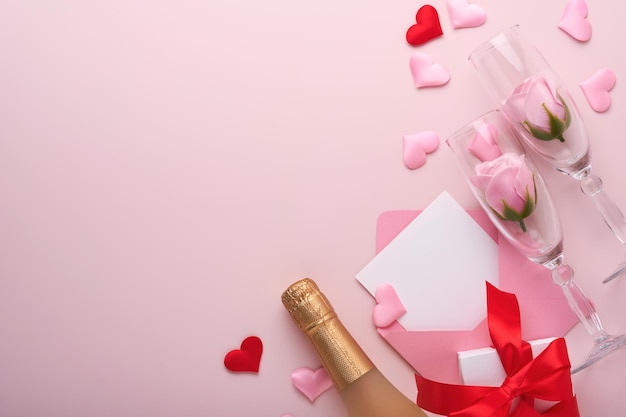 Cartolina d'auguri di San Valentino con bottiglia di champagne, confezione regalo, nastro rosso e busta con mockup di note vuote all'interno su sfondo rosa. Vista dall'alto con spazio per i saluti. Biglietto di auguri con spazio per la copia