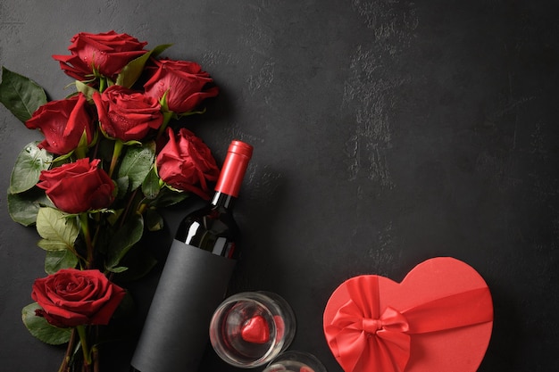 Cartolina d'auguri di San Valentino con rose rosse e regalo di vino e cuori su sfondo nero con spazio di copia.