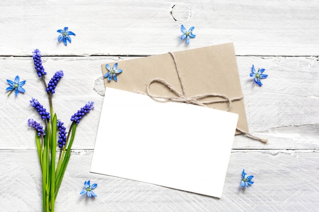 Cartolina d'auguri e busta bianche in bianco con il mazzo e i germogli dei fiori blu della molla