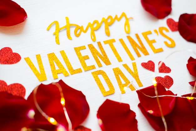 Cartolina d'auguri felice del testo di San Valentino con il fondo di legno bianco dei petali di rosa rossa e del heartson. concetto romantico e d'amore