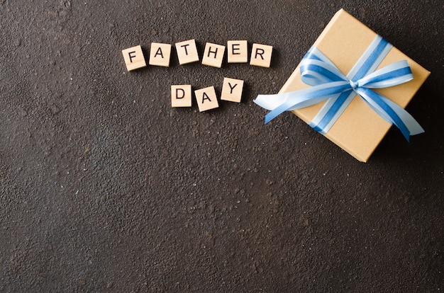 Cartolina d'auguri felice di festa del papà con il contenitore di regalo decorato su fondo scuro.