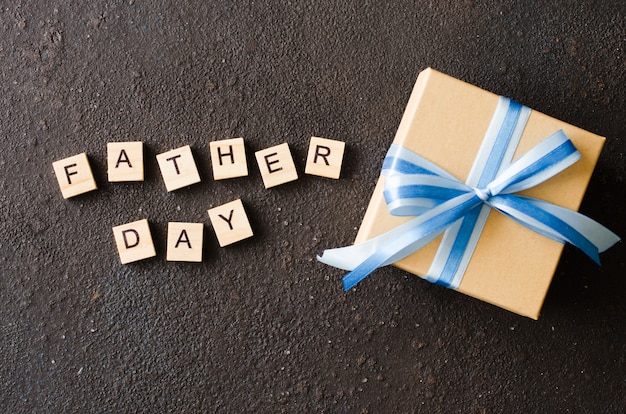 Cartolina d'auguri felice di festa del papà con il contenitore di regalo decorato su fondo scuro.