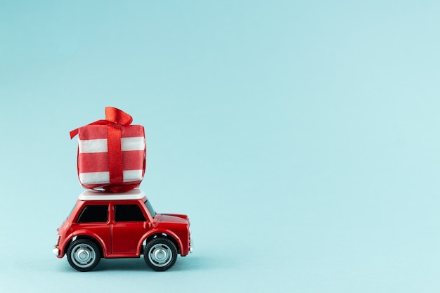 Cartolina d'auguri festiva di Natale con il contenitore di regalo di trasporto dell'automobile rossa del giocattolo sull'azzurro