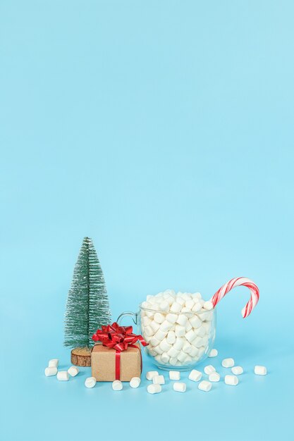 Cartolina di buon natale e felice anno nuovo. Confezione regalo, albero di natale e tazza di marshmallow con canna da lecca-lecca rossa su sfondo blu. Concetto di vacanza. Vista frontale, spazio della copia della cartolina d'auguri.