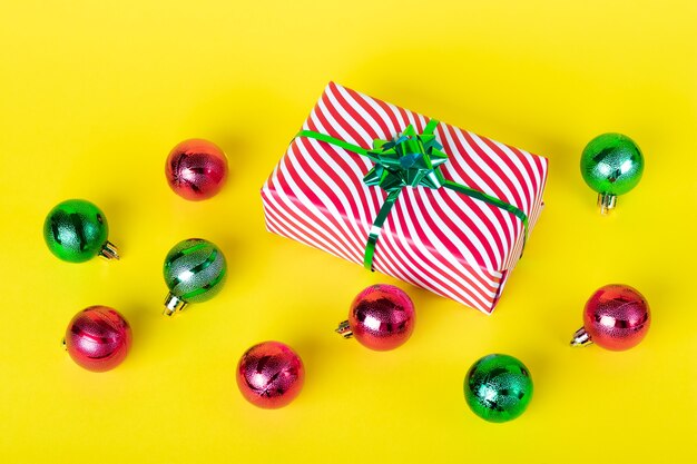 Cartolina di Natale con confezione regalo e palline lucide su una parete gialla.