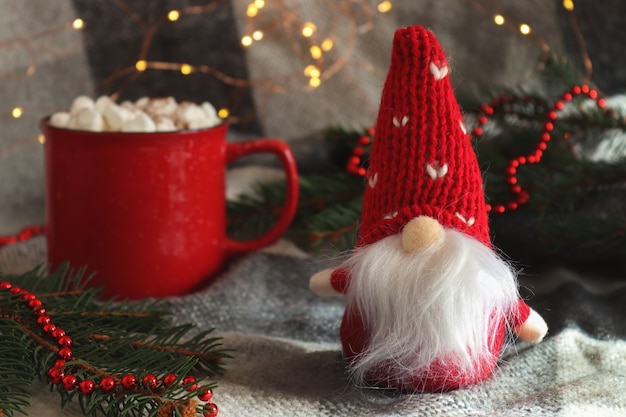 Cartolina di Natale divertente con gnomo giocattolo una tazza di cioccolata calda con marshmallow e rami di abete