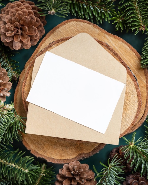 Cartolina di Natale e busta in bianco tra rami di abete e pigne sul verde da vicino