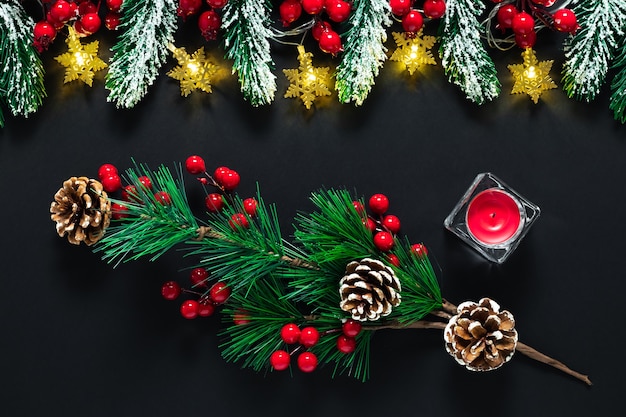 Cartolina di Natale nera, sfondo di Capodanno con rami di abete verde, pigne, bacche rosse e candela.