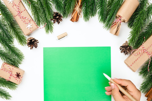 Cartolina di Natale verde lettera con copia spazio e una mano di donna con penna artigianale sul tavolo bianco e o...