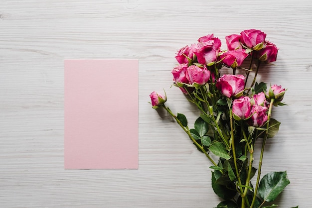 Cartolina rosa artigianale con bouquet di roselline su fondo in legno Spazio per messaggi di testo Fiori primaverili Biglietto di auguri per le vacanze per San Valentino Festa della mamma delle donne Pasqua Vista dall'alto piatta