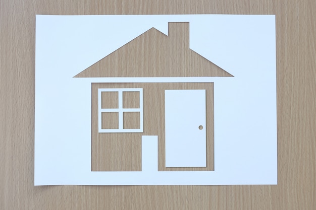 Casa a forma di carta su uno sfondo di legno marrone.