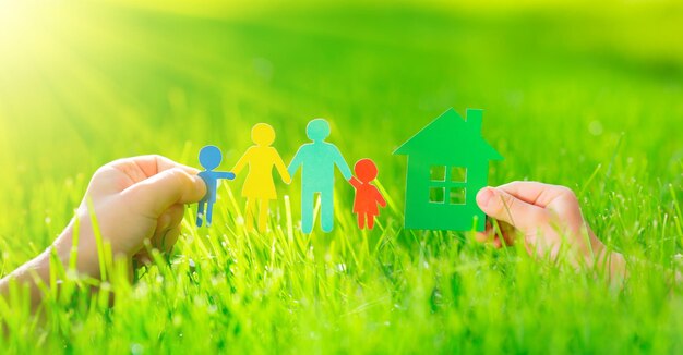 Casa di carta e famiglia nelle mani sull'erba verde primaverile Concetto di ecologia