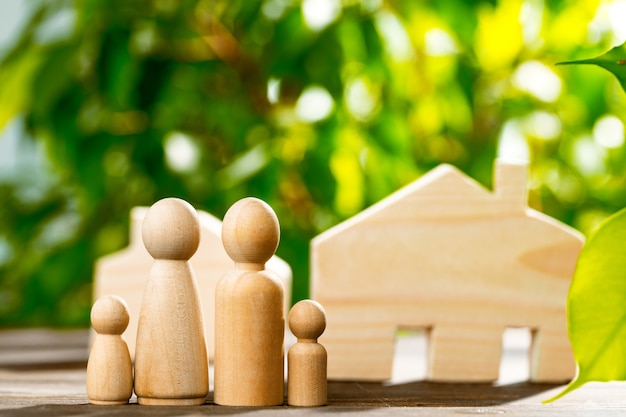 Casa di legno del giocattolo e famiglia di legno sulla fine del fondo del fogliame su