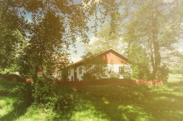 Casa di legno rossa svedese tradizionale con il cielo blu del recinto e gli alberi alla priorità bassa dei pantaloni a vita bassa dell'annata naturale di vacanza di festa di primavera