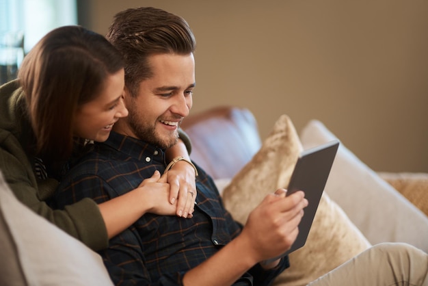 Casa e coppia abbracciare con tablet sorriso e social media post con romanticismo e rilassarsi in salotto appartamento abbracciare e donna con l'uomo e la tecnologia con lettura online e app digitale con commedia e amore