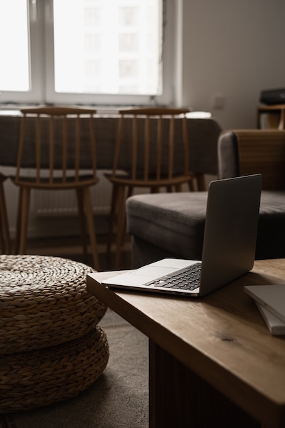 Casa estetica minimale, interior design del soggiorno. Tavolo in legno con computer portatile, pouf in rattan, sgabelli