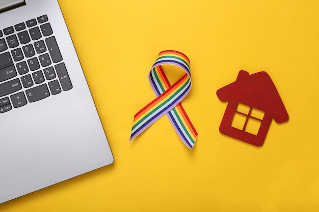 Casa giocattolo e laptop con nastro arcobaleno lgbt su sfondo giallo Tolleranza al concetto di comunità di persone omosessuali e bisessuali