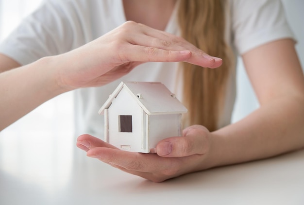 Casa giocattolo in legno protetta dalle mani Concetto di assicurazione sulla casa