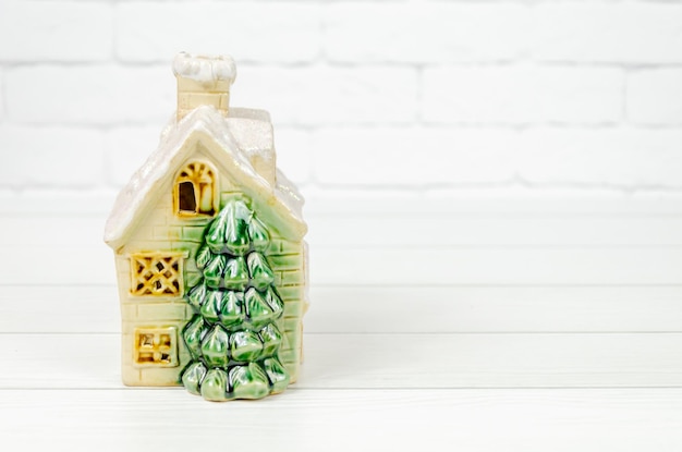Casa in ceramica con albero di Natale su sfondo bianco casa giocattolo vintage con tetto innevato
