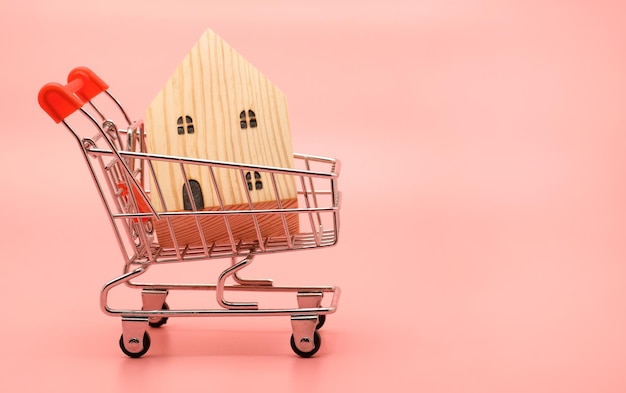 Casa in legno decorativo in miniatura nel carrello sul concetto rosa di vendita e acquisto immobiliare