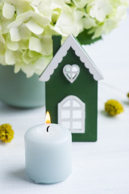 Casa in legno verde bianca, fiori di ortensie in vaso e candele accese