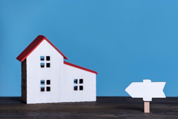 Casa in miniatura con cartello in legno Concetto di casa propria Vista frontale su sfondo blu