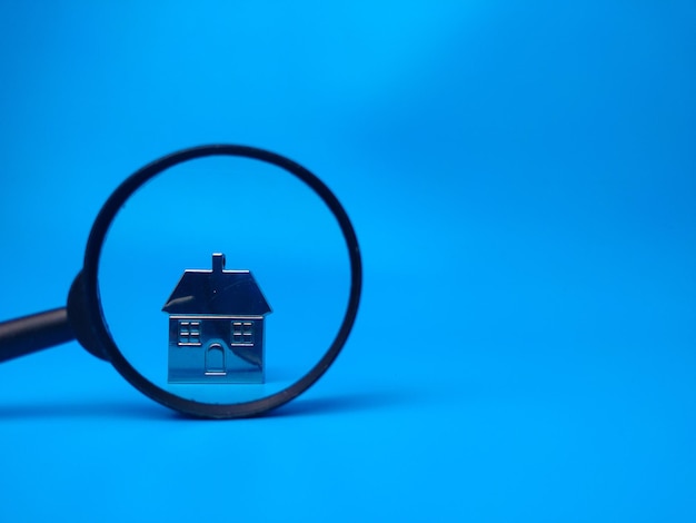 Casa in miniatura e lente d'ingrandimento su sfondo blu con copia spaceReal estate concetto