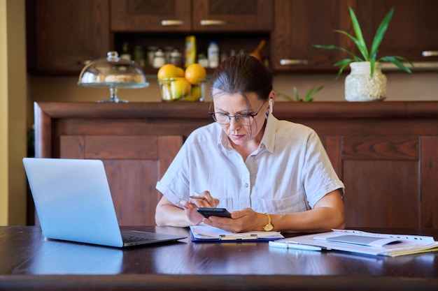 Casa sul posto di lavoro donna di mezza età in cuffia che lavora utilizzando il computer portatile