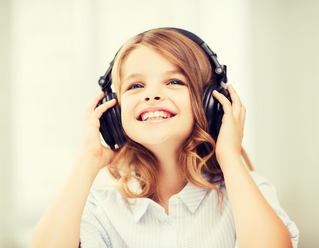 casa, tempo libero, nuova tecnologia e concetto di musica - bambina sorridente con le cuffie a casa