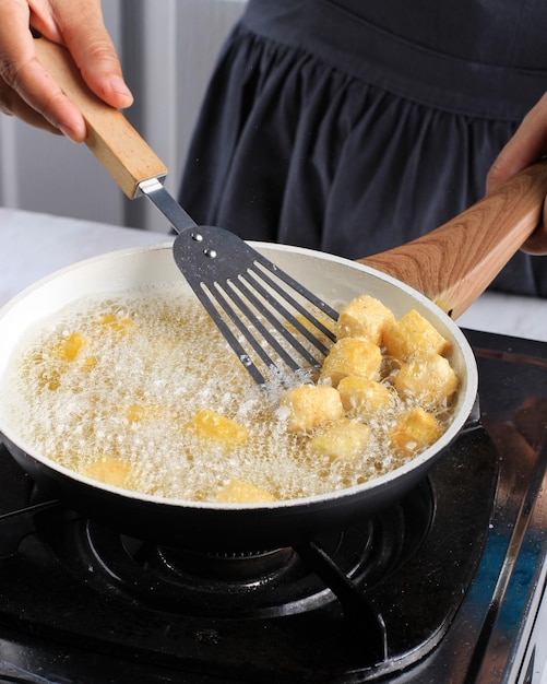 Casalinga asiatica che frigge il tofu sull'olio bollente, usando il gas Stoce in cucina. Processo di cottura dietro le quinte