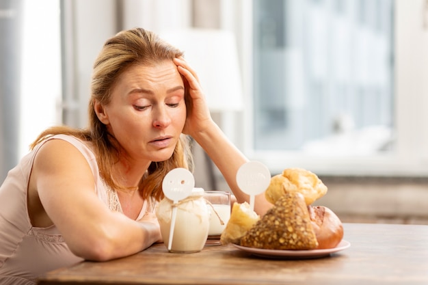 Casalinga bionda matura seduta al tavolo e guardando cibi che evocano allergie