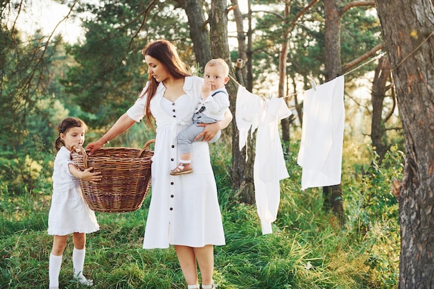 Casalinga che asciuga i vestiti Giovane madre con la sua piccola figlia e figlio è all'aperto nella foresta Bel sole